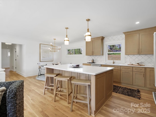 kitchen featuring light wood finished floors, a kitchen island, light countertops, a kitchen breakfast bar, and backsplash