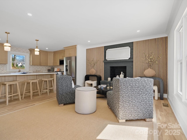 living area featuring visible vents, recessed lighting, ornamental molding, light wood-style floors, and a brick fireplace