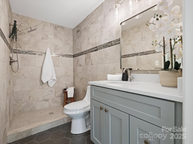 full bath with tile patterned floors, toilet, a tile shower, tile walls, and vanity