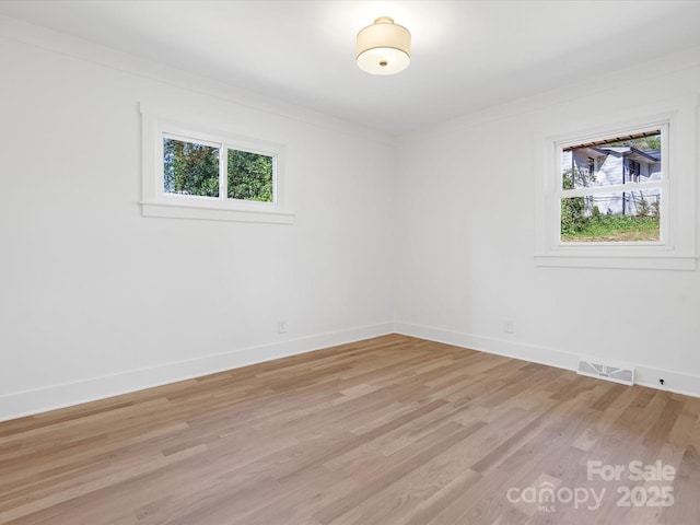 spare room with crown molding, light wood-style flooring, baseboards, and visible vents