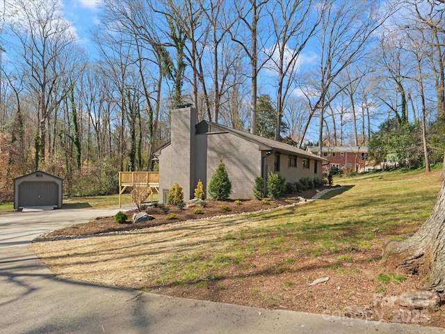 view of property exterior featuring a detached garage, concrete driveway, a chimney, a yard, and an outbuilding