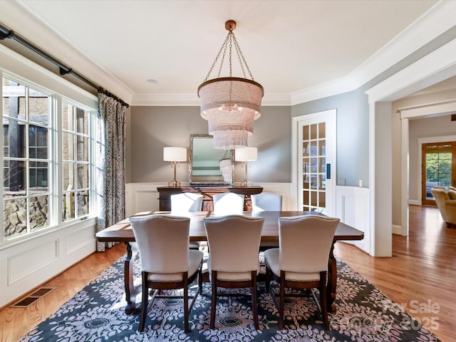 dining room with a wainscoted wall, crown molding, visible vents, and a chandelier