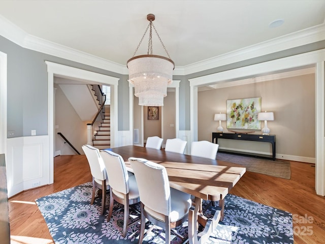 dining area with stairway, a notable chandelier, wood finished floors, and ornamental molding