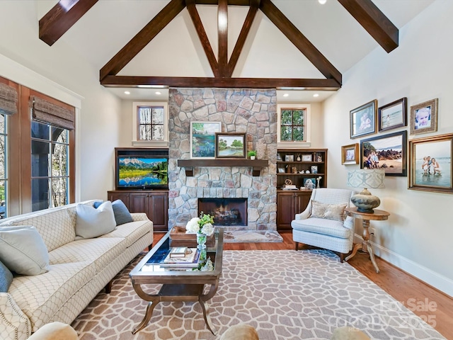 living area with beam ceiling, high vaulted ceiling, a stone fireplace, and wood finished floors