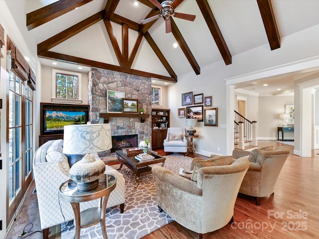 living area with wood finished floors, high vaulted ceiling, beam ceiling, a stone fireplace, and stairs