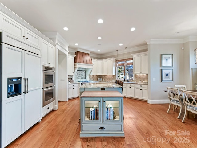 kitchen with custom range hood, ornamental molding, white cabinets, and stainless steel appliances