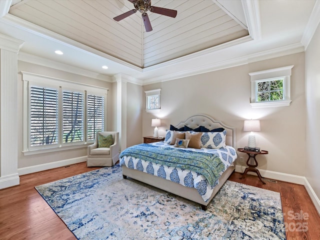 bedroom featuring a raised ceiling, crown molding, baseboards, and wood finished floors