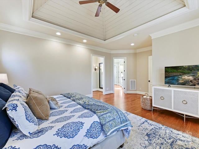 bedroom featuring a tray ceiling, crown molding, wood finished floors, and visible vents