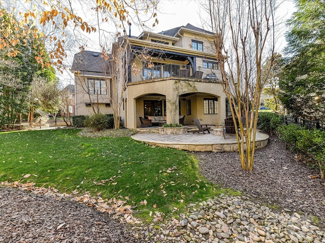 back of property featuring stucco siding, a balcony, a lawn, and fence