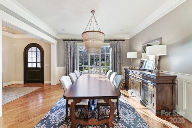 dining room featuring a wainscoted wall, arched walkways, light wood-style flooring, and crown molding