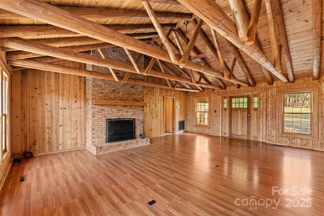 unfurnished living room featuring light wood-style floors, wooden ceiling, wood walls, a brick fireplace, and vaulted ceiling with beams