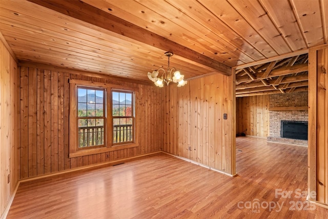 spare room with wooden ceiling, light wood-style flooring, a fireplace, and a chandelier