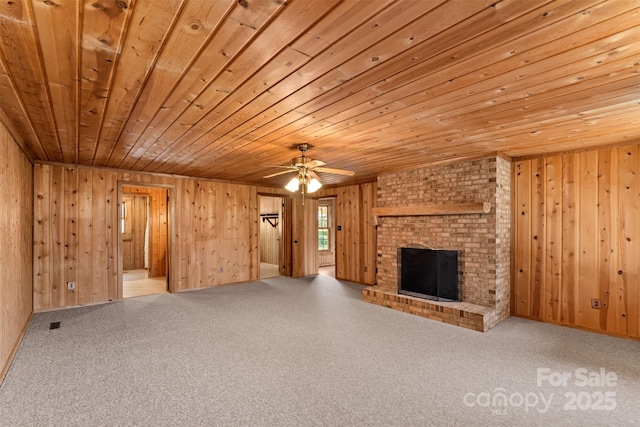 unfurnished living room with a ceiling fan, wooden walls, wooden ceiling, carpet flooring, and a fireplace