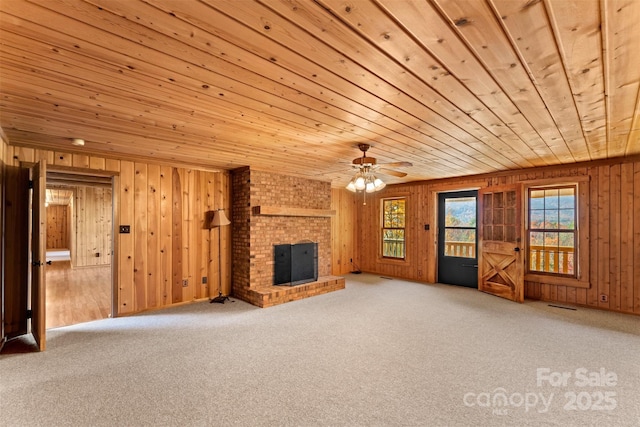 unfurnished living room featuring visible vents, wooden walls, wooden ceiling, carpet flooring, and a brick fireplace