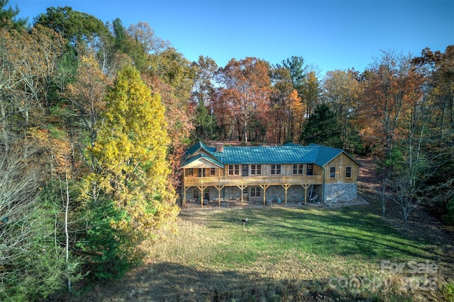 view of front of house featuring a front yard, a forest view, stone siding, a deck, and metal roof