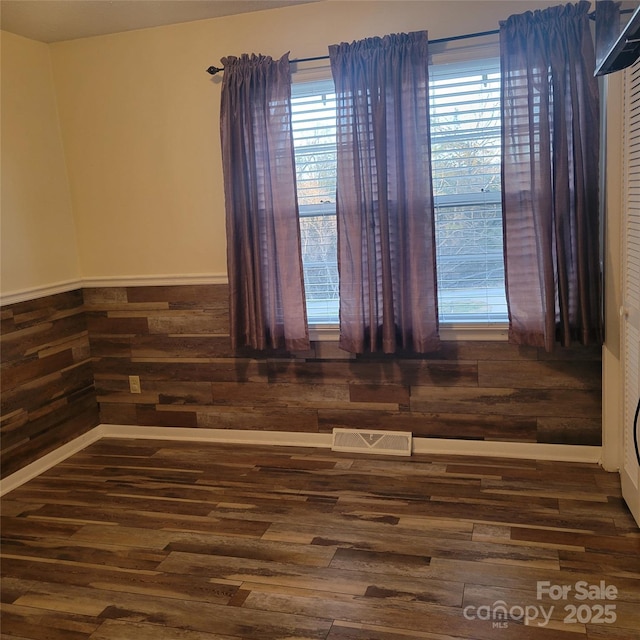 unfurnished room with wainscoting, visible vents, wooden walls, and wood finished floors