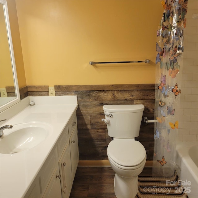 bathroom featuring wainscoting, toilet, wood finished floors, shower / bath combination with curtain, and vanity