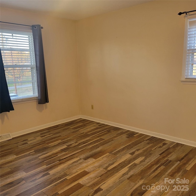 empty room with dark wood-style flooring, visible vents, and baseboards