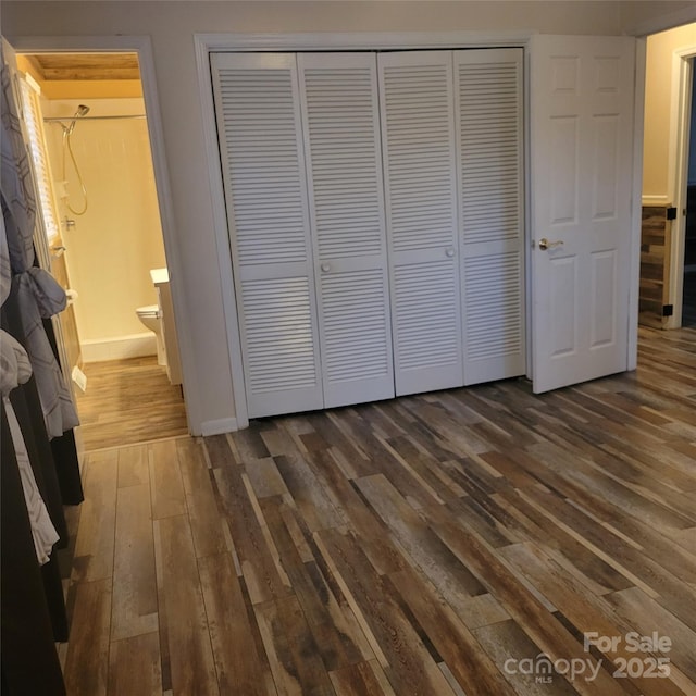 unfurnished bedroom with dark wood-style floors, a closet, and ensuite bath