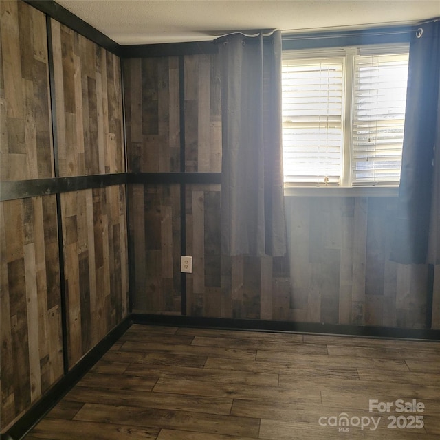 unfurnished room with wood walls and dark wood-type flooring