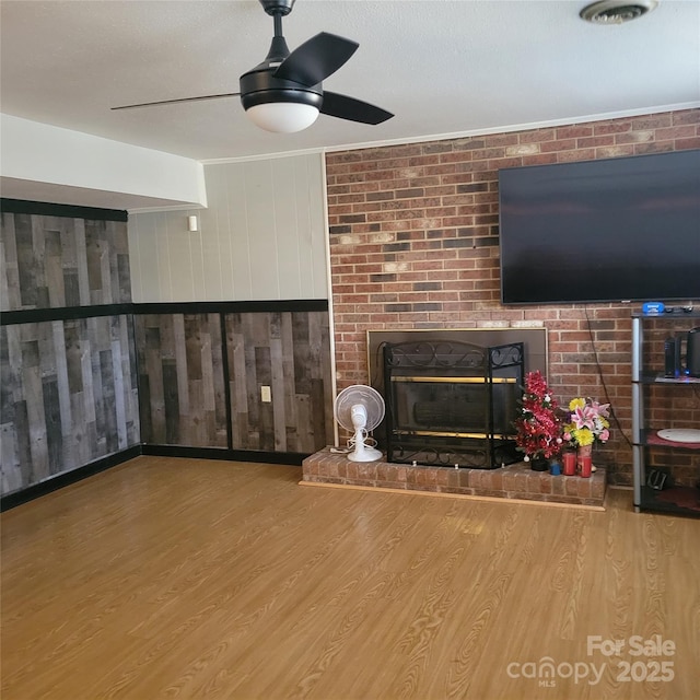 unfurnished living room featuring ceiling fan, a fireplace, ornamental molding, and wood finished floors