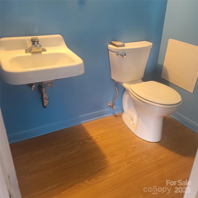 half bathroom with a sink, wood finished floors, toilet, and baseboards