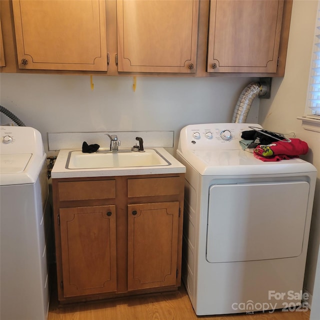 washroom with washing machine and dryer, cabinet space, a sink, and light wood-style flooring