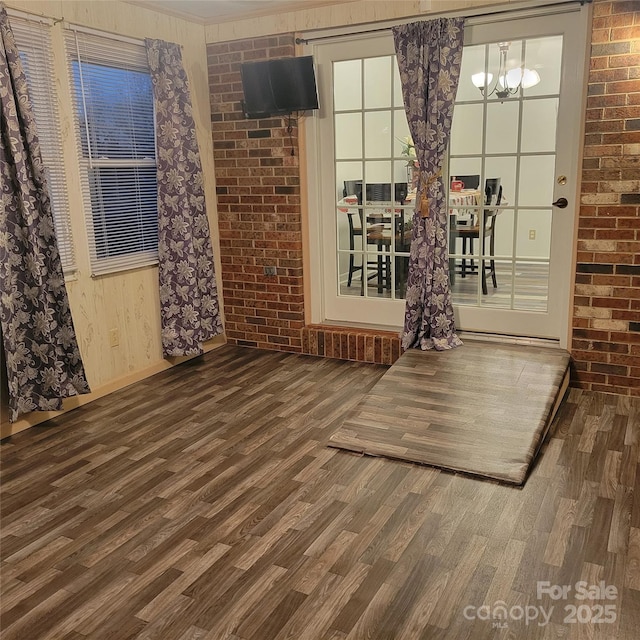 unfurnished room featuring brick wall, a chandelier, and wood finished floors