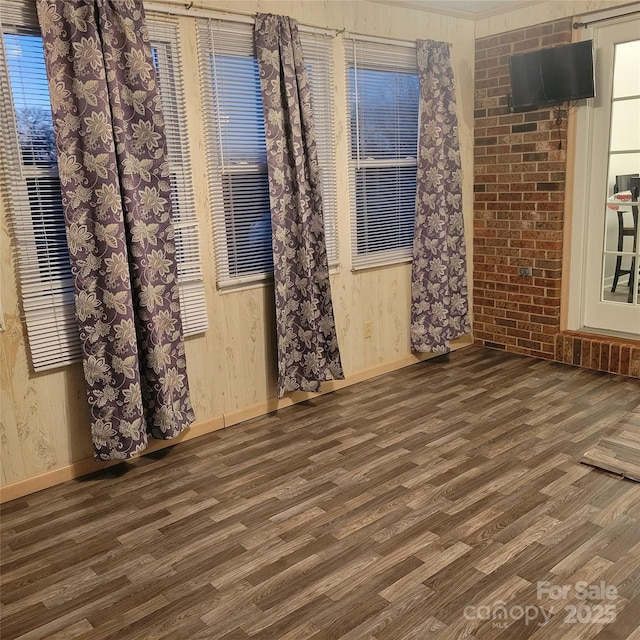 spare room featuring brick wall, baseboards, and wood finished floors