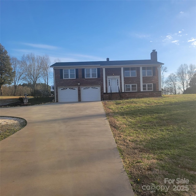 split foyer home with concrete driveway, a chimney, an attached garage, a front lawn, and brick siding