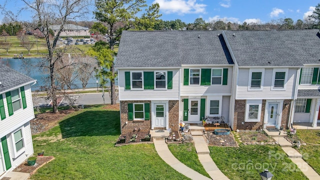 townhome / multi-family property featuring brick siding, a front lawn, and roof with shingles