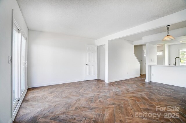 unfurnished room featuring a sink, baseboards, and a textured ceiling