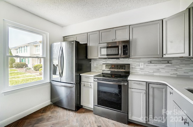 kitchen featuring backsplash, appliances with stainless steel finishes, gray cabinetry, and light countertops