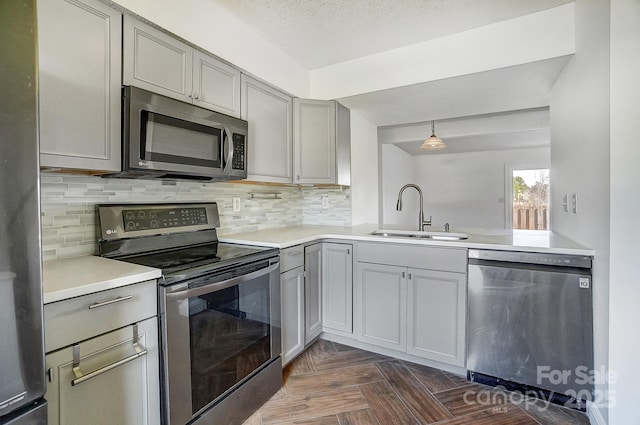 kitchen featuring tasteful backsplash, light countertops, gray cabinets, appliances with stainless steel finishes, and a sink