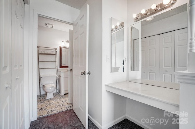 bathroom featuring vanity, toilet, baseboards, and a closet