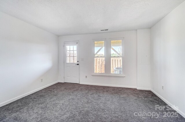 spare room featuring dark colored carpet, visible vents, baseboards, and a textured ceiling