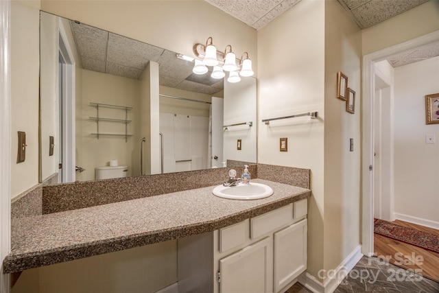 full bathroom featuring a drop ceiling, toilet, vanity, and baseboards