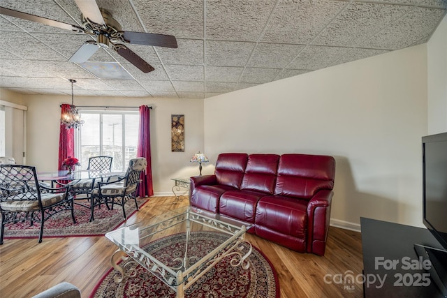 living room featuring ceiling fan with notable chandelier, baseboards, and wood finished floors