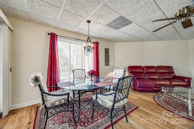 dining room featuring a drop ceiling, baseboards, wood finished floors, and ceiling fan with notable chandelier