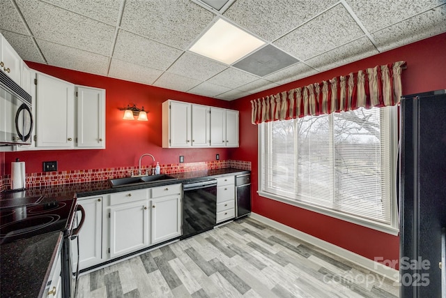 kitchen featuring a sink, black appliances, white cabinets, dark countertops, and light wood-type flooring