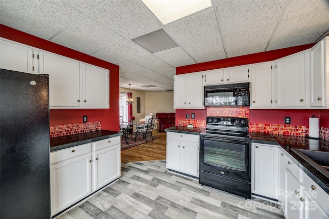 kitchen featuring light wood-type flooring, dark countertops, black appliances, and white cabinetry