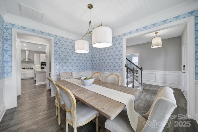 dining space with wallpapered walls, a wainscoted wall, wood finished floors, and visible vents