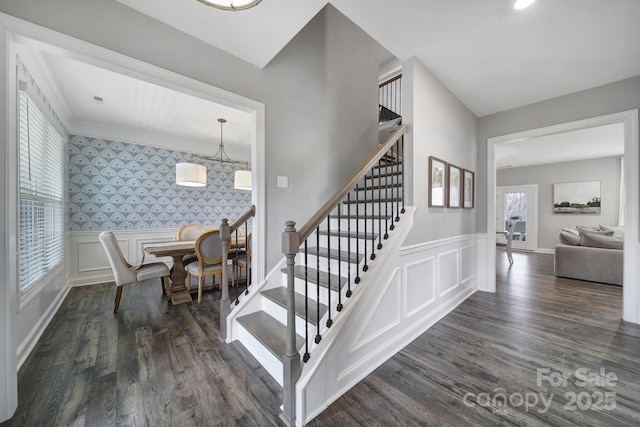 stairs with wallpapered walls, wood finished floors, a wainscoted wall, and a chandelier