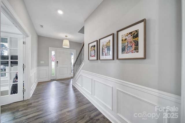 foyer with visible vents, a wainscoted wall, dark wood-type flooring, a decorative wall, and stairs