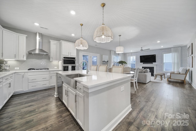 kitchen featuring double oven, wall chimney exhaust hood, dark wood-style flooring, and a sink