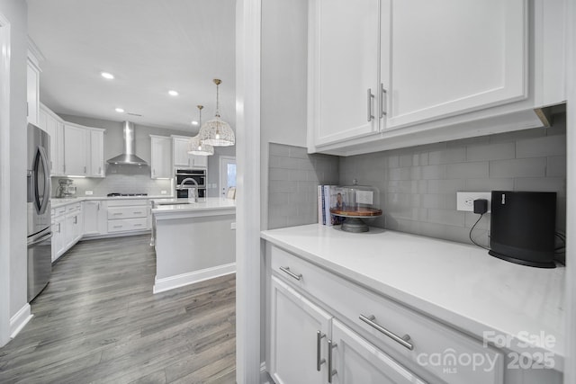 kitchen featuring white cabinetry, wood finished floors, stainless steel refrigerator, and wall chimney range hood