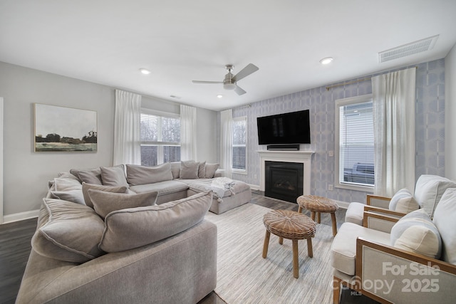 living area with a ceiling fan, visible vents, baseboards, a fireplace, and dark wood-style flooring