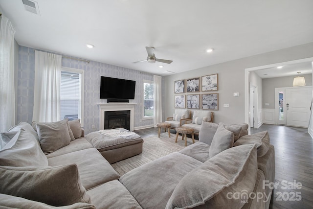 living room featuring a glass covered fireplace, wood finished floors, visible vents, and ceiling fan