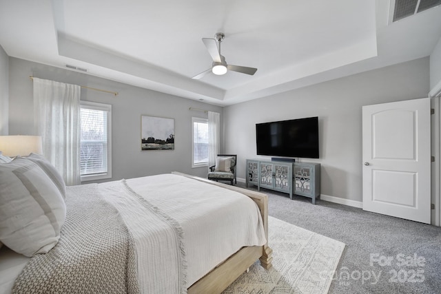 carpeted bedroom with a ceiling fan, a tray ceiling, baseboards, and visible vents