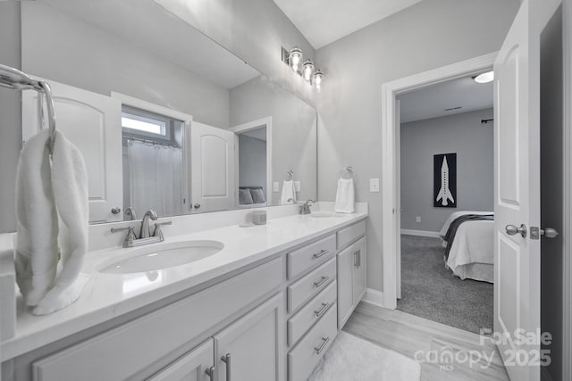 ensuite bathroom featuring double vanity, connected bathroom, baseboards, and a sink